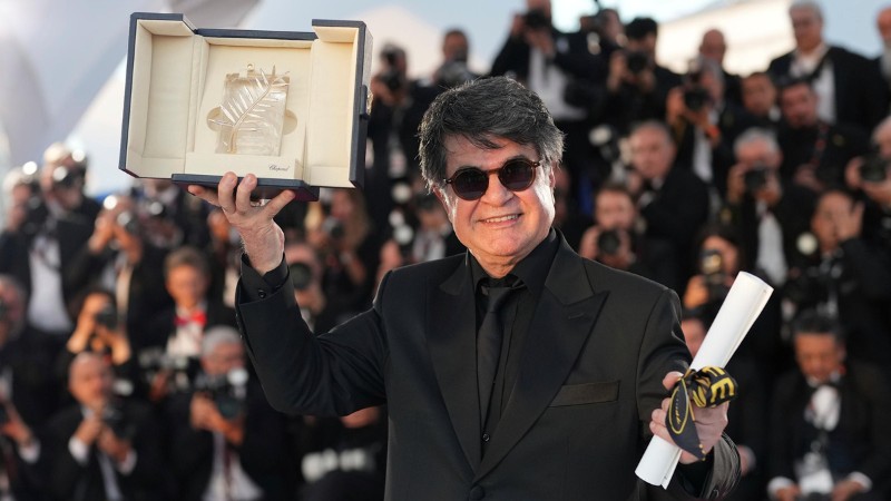 Jafar Panahi holding the Palme d'Or at Cannes 2025, surrounded by photographers